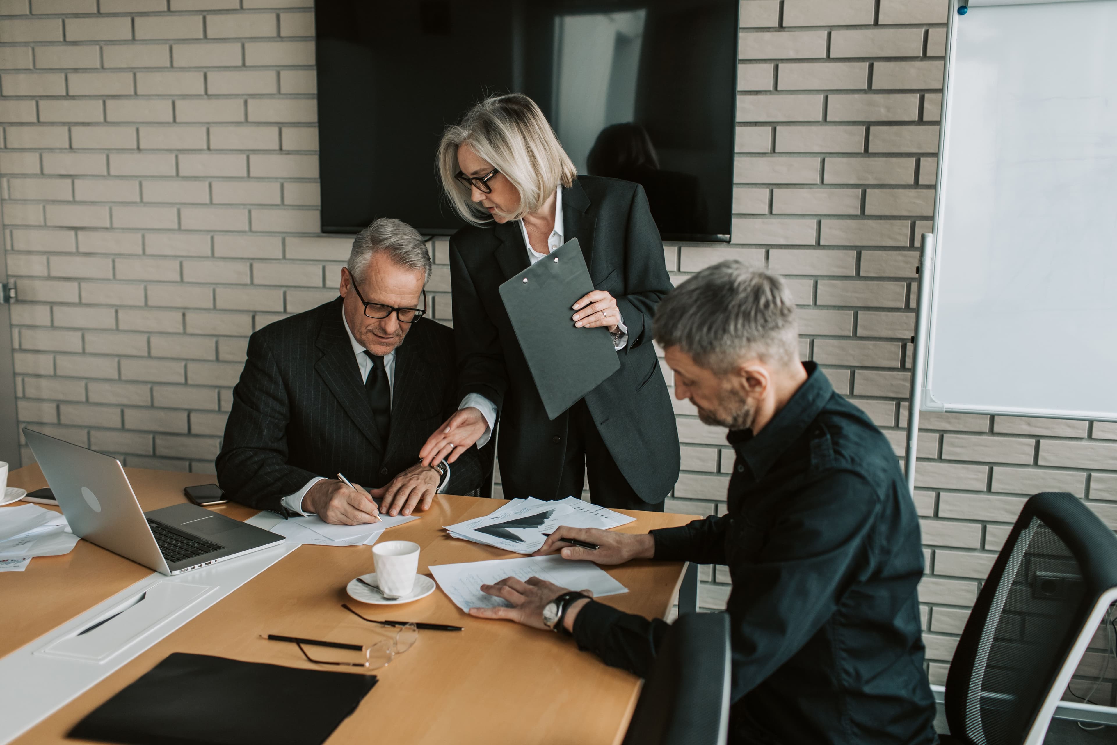 Three executives reviewing documents and printed charts at a conference table