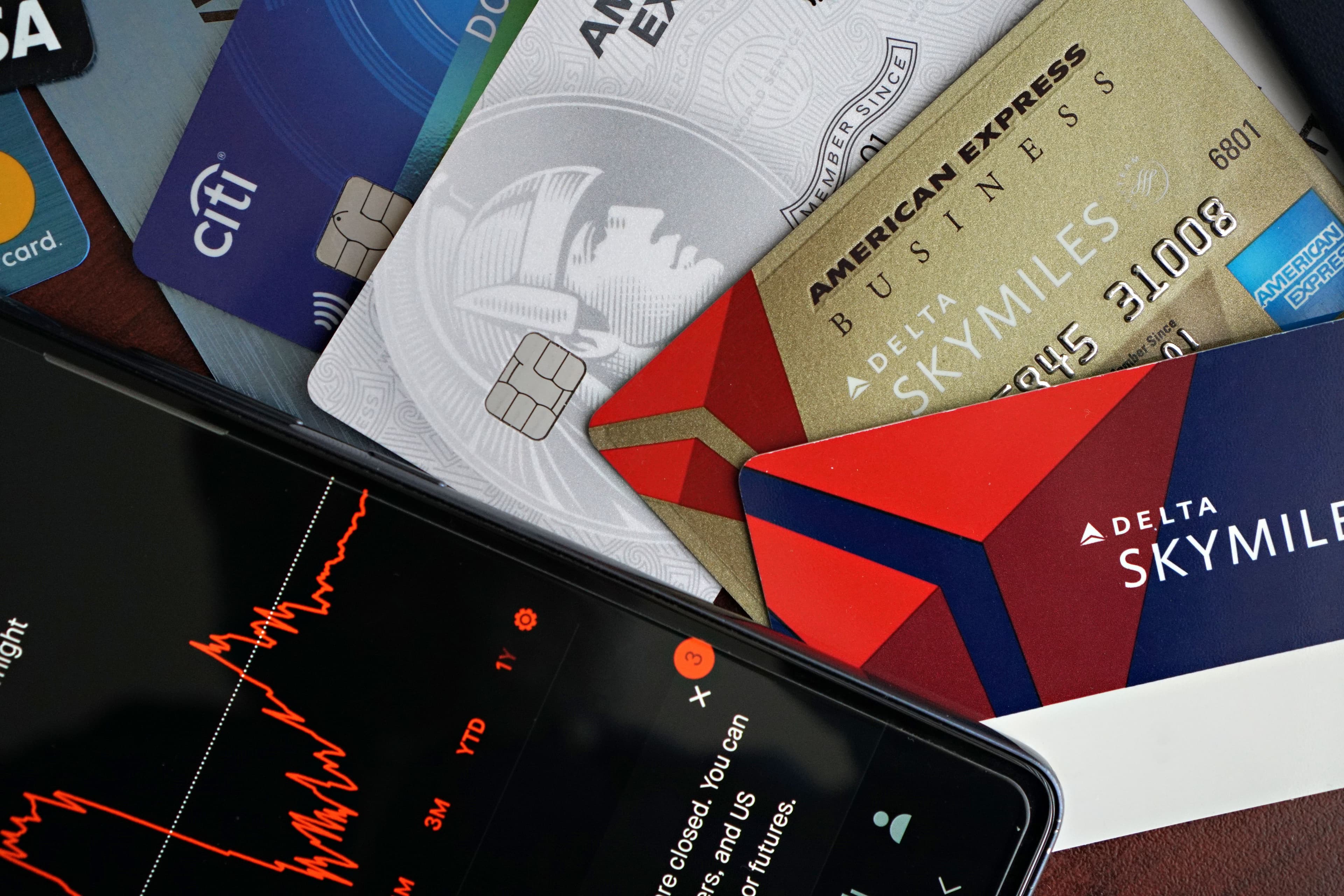 A fan of credit cards next to a phone showing a stock trading chart