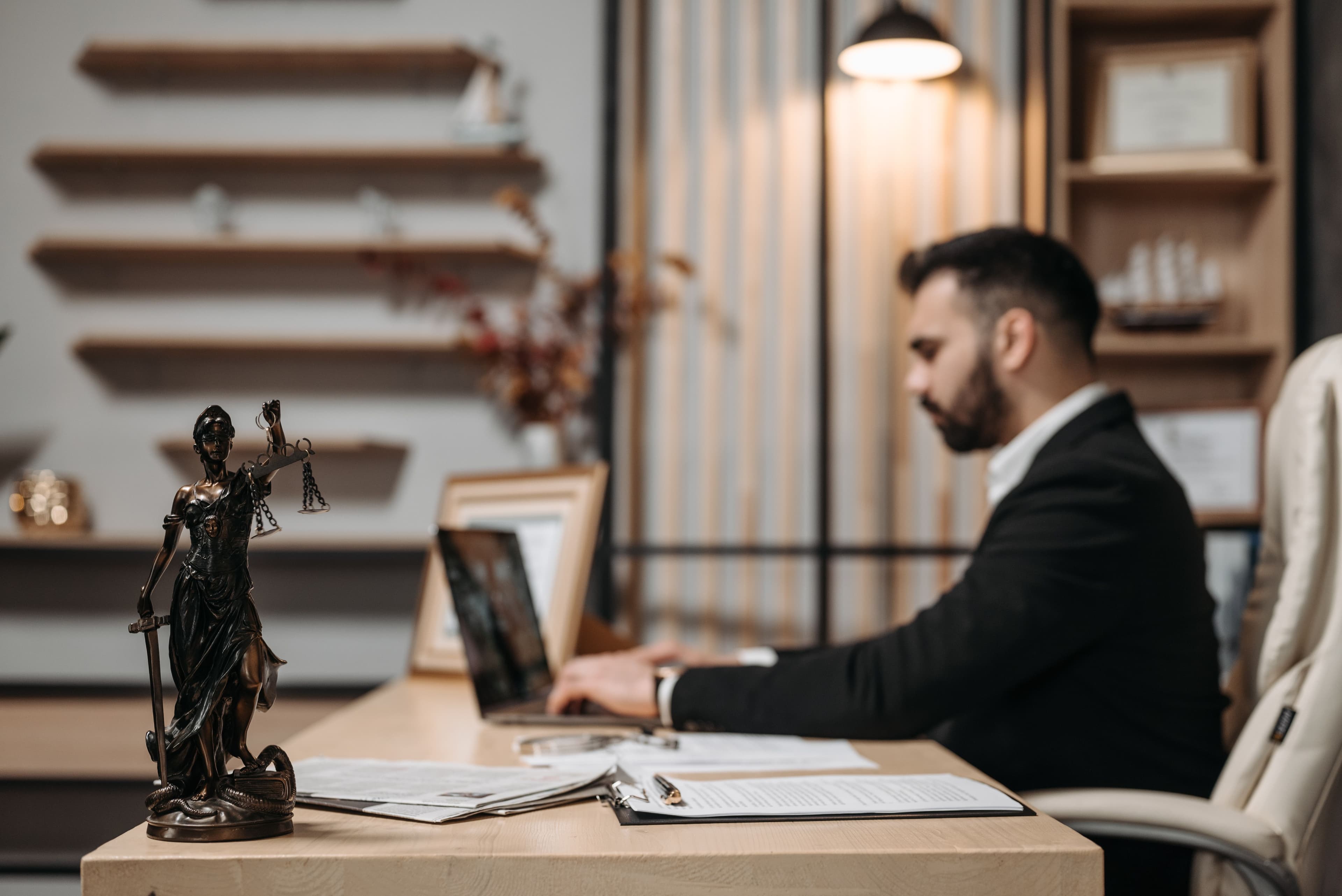 A lawyer working at a laptop at his desk, with a statue of Lady Justice in the foreground
