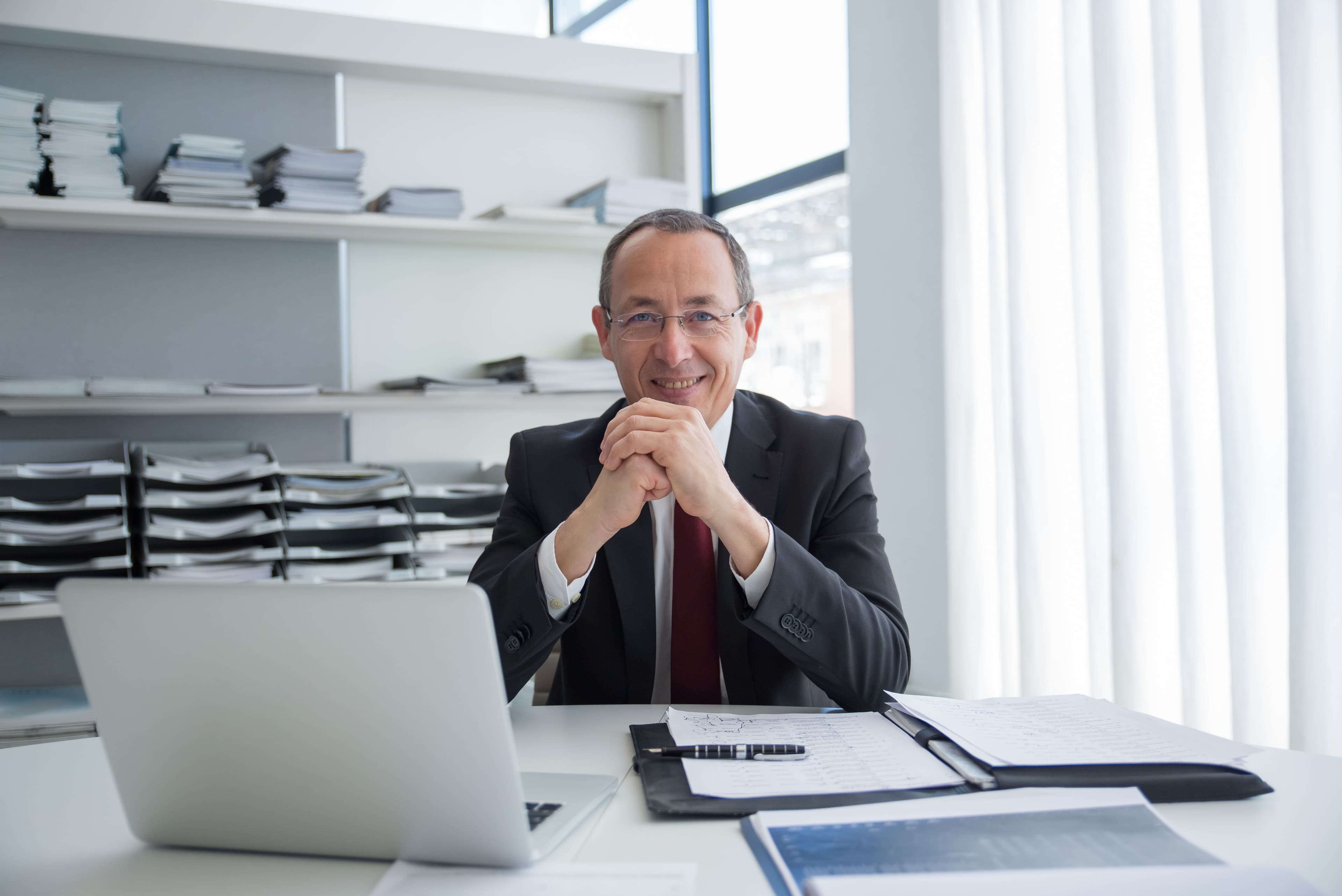 Smiling executive at a desk with a laptop and printed reports